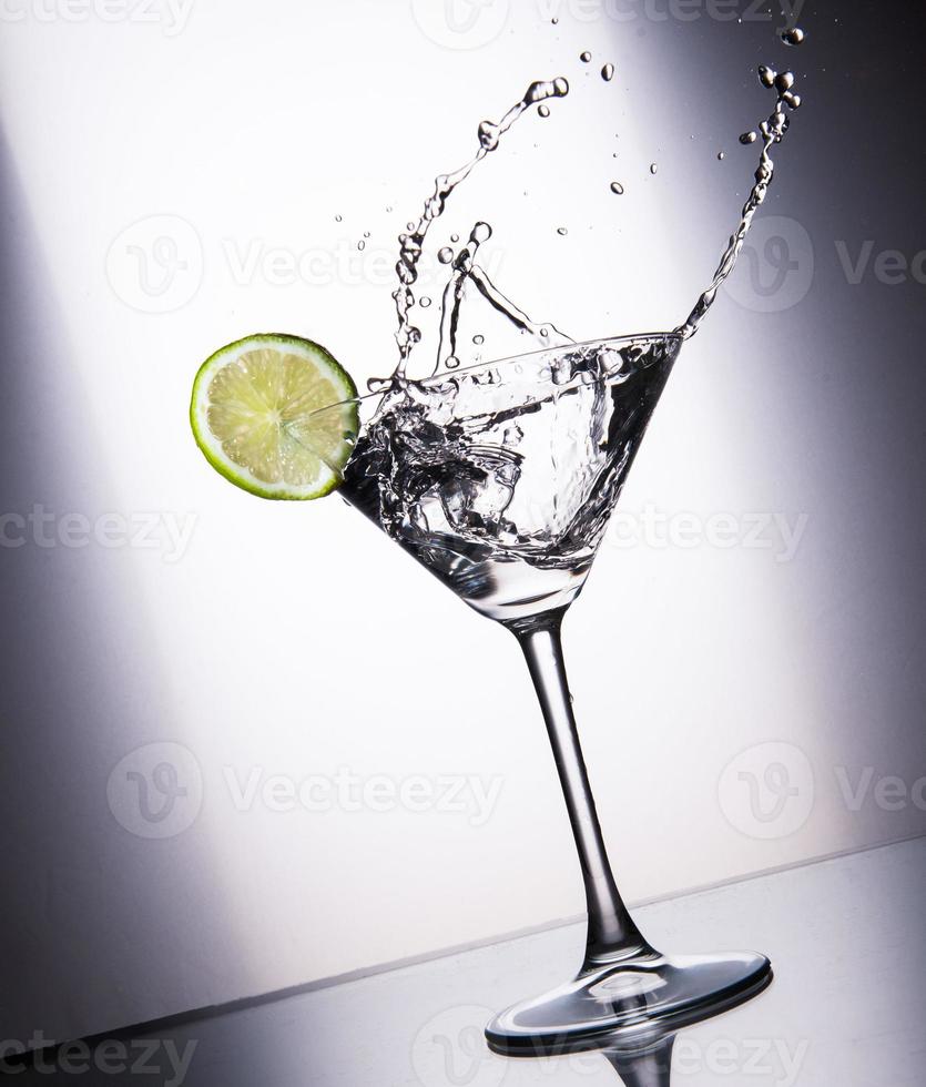 Cocktail glass with juice, lime and ice splashing photo