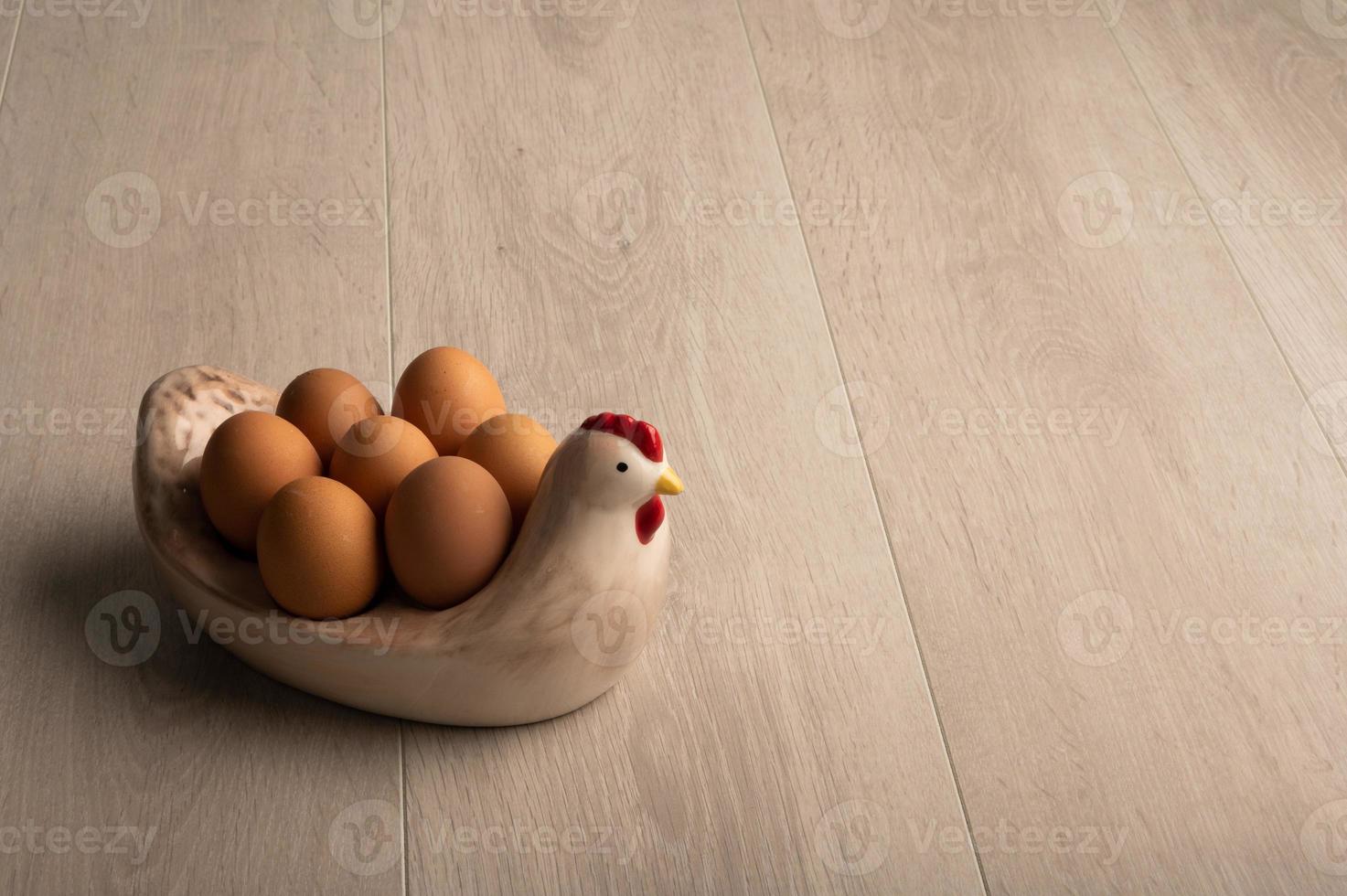 Eggs on a chicken shaped bowl a light wood background and room for copy photo