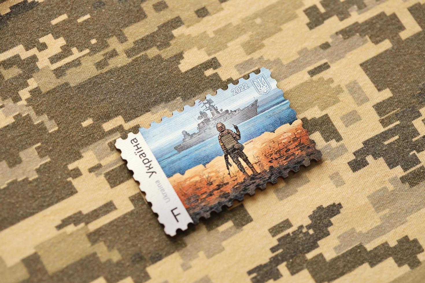 TERNOPIL, UKRAINE - SEPTEMBER 2, 2022 Famous Ukrainian postmark with russian warship and ukrainian soldier as wooden souvenir on army camouflage uniform photo