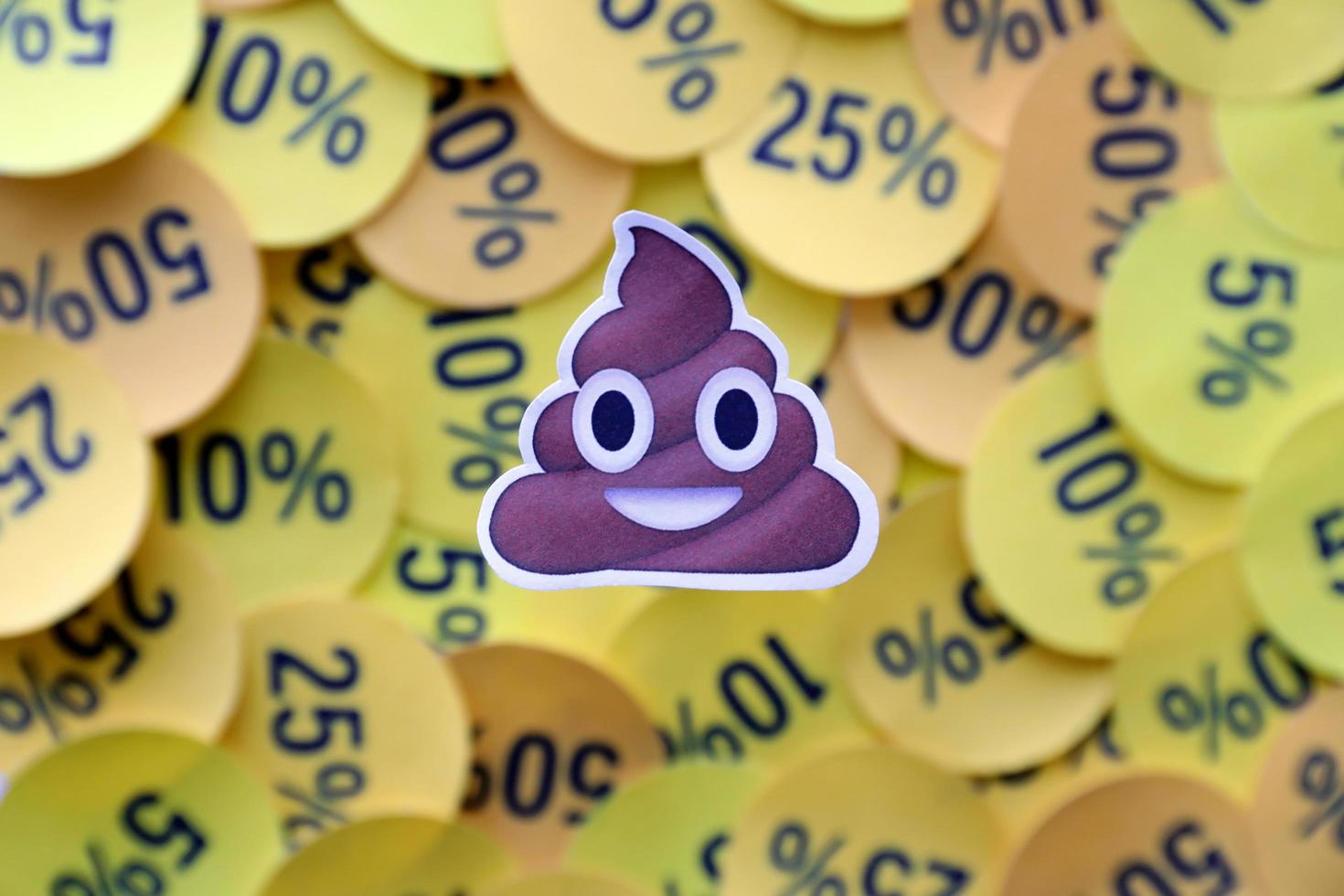 Ternopil, Ukraine - May 8, 2022 Shit emoji sticker on large amount of yellow stickers with percentage values for black friday or cyber monday photo