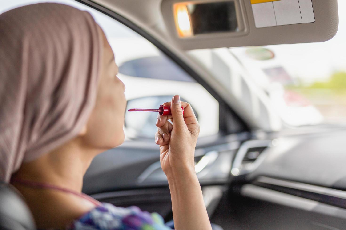 Woman looking in rear view mirror painting her lips doing applying make up in car. photo
