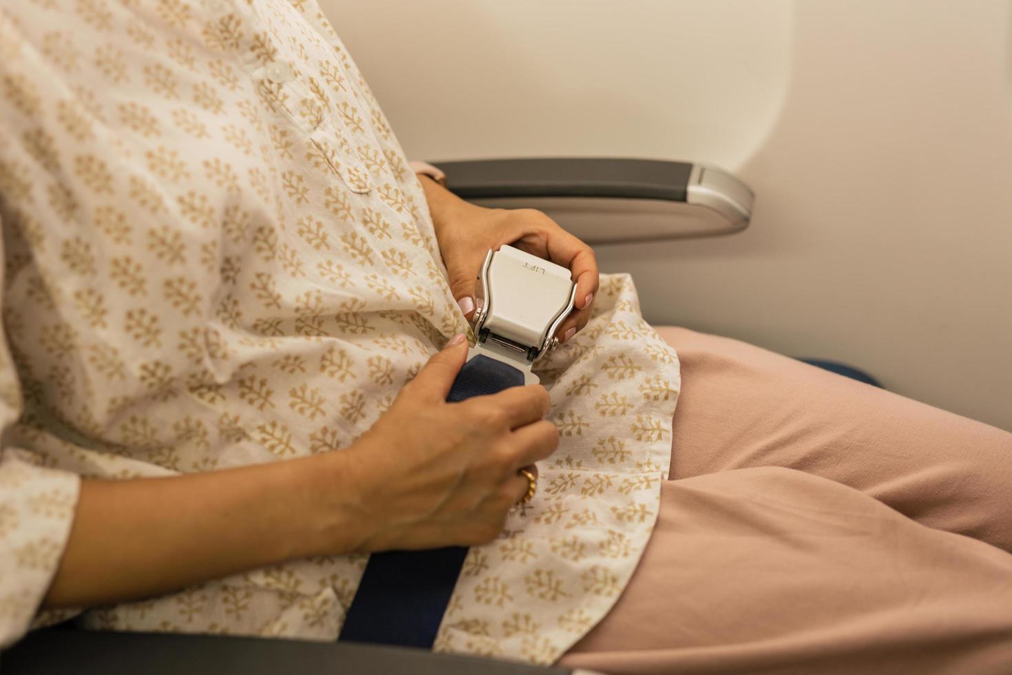 Woman fastens seat belt while sitting in a passenger airplane chair by the window. photo