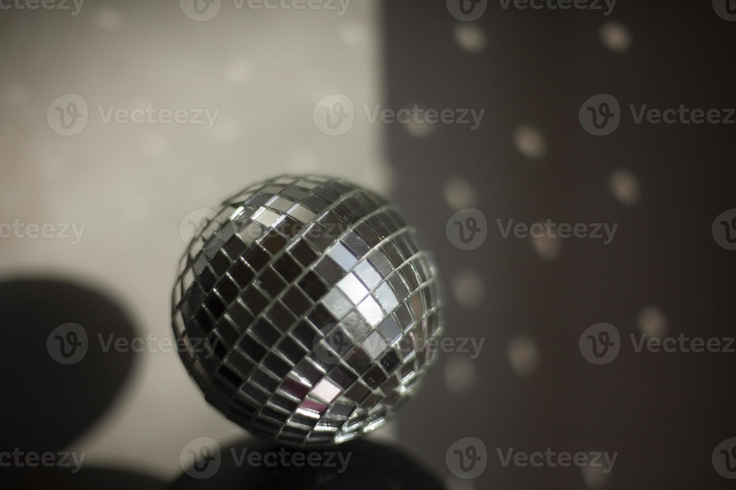 Disco ball reflects light in room. Ball of small mirrors stands on surface of speaker. photo