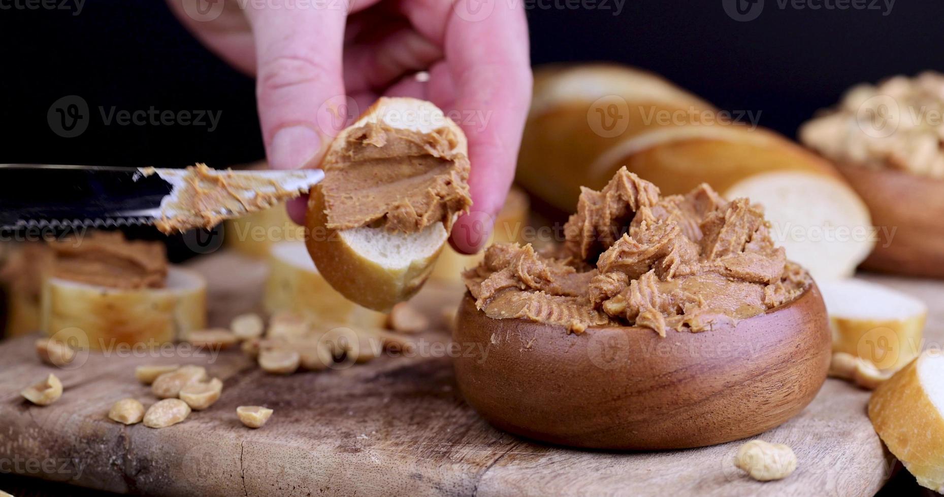 spread peanut butter with pieces of nuts on a fresh white baguette photo