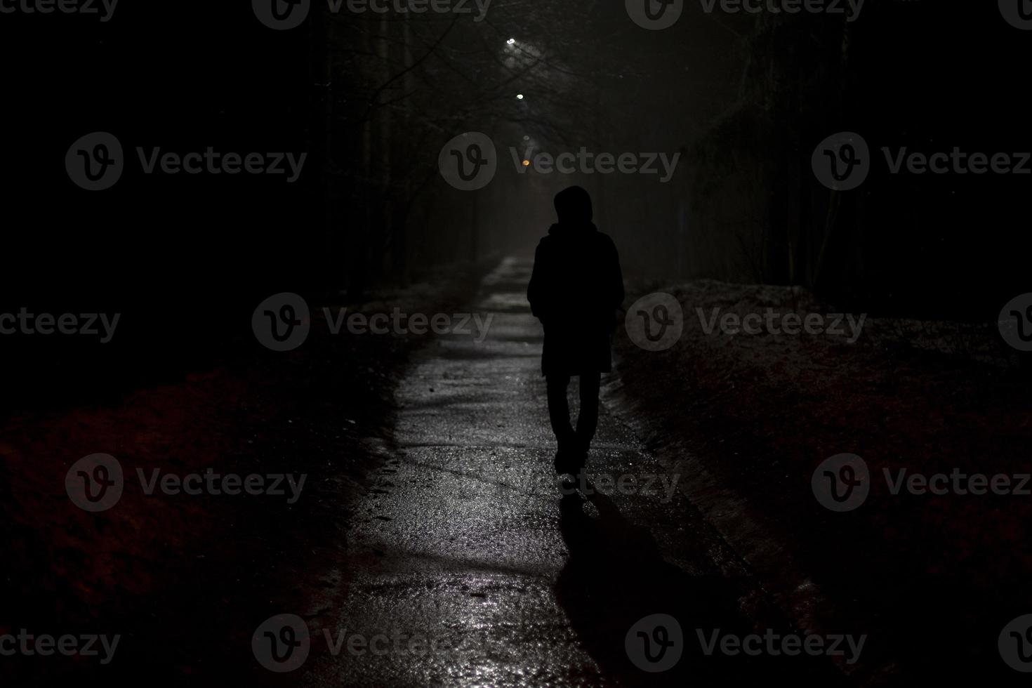 Silhouette of man at night in park. Man walks alone on road in evening. photo