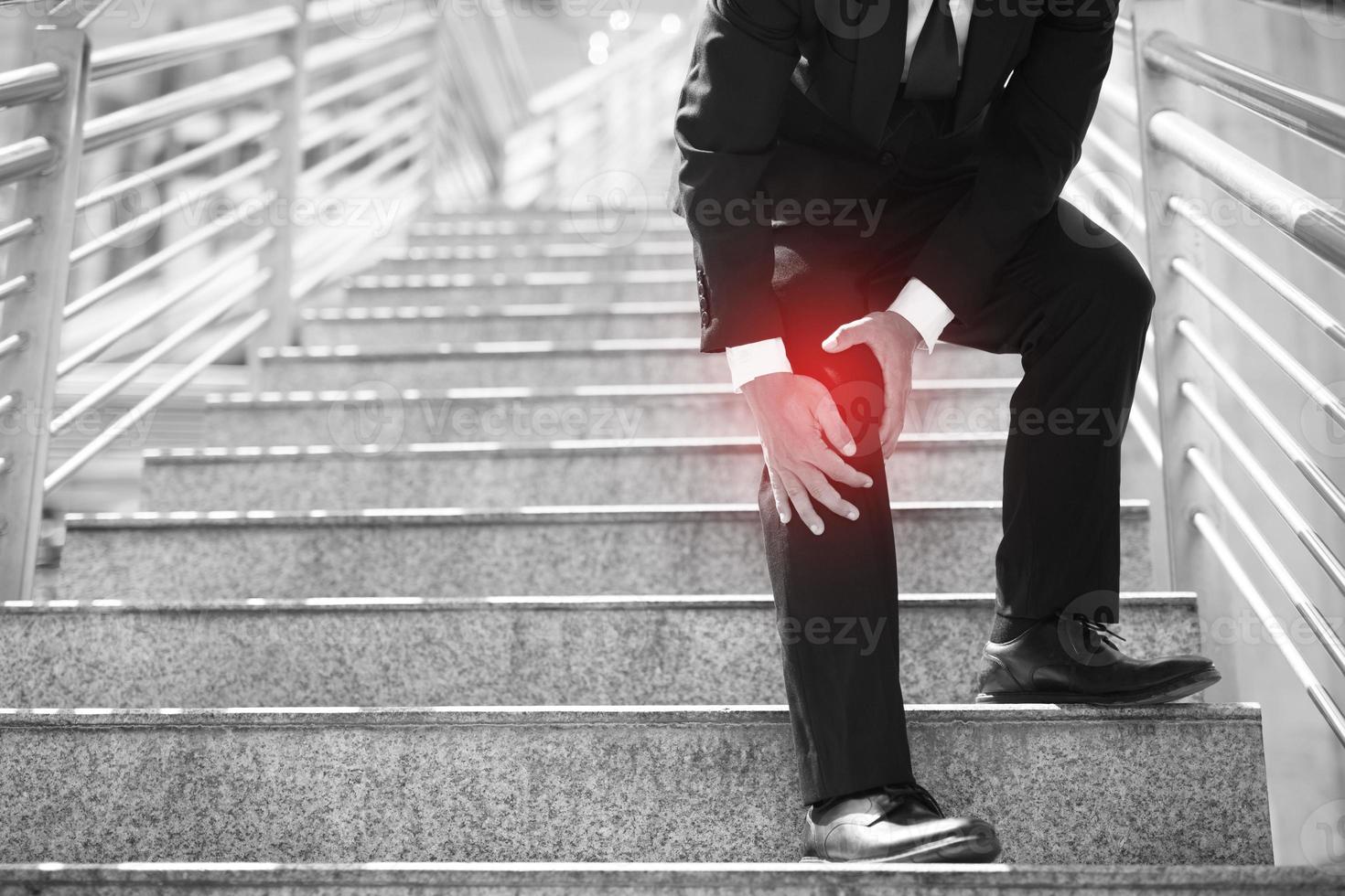 el hombre de negocios con traje tiene el dolor dolorido y la expresión dolorosa del problema de la rodilla y sube y baja la escalera mientras va a la oficina. concepto de atención médica. foto