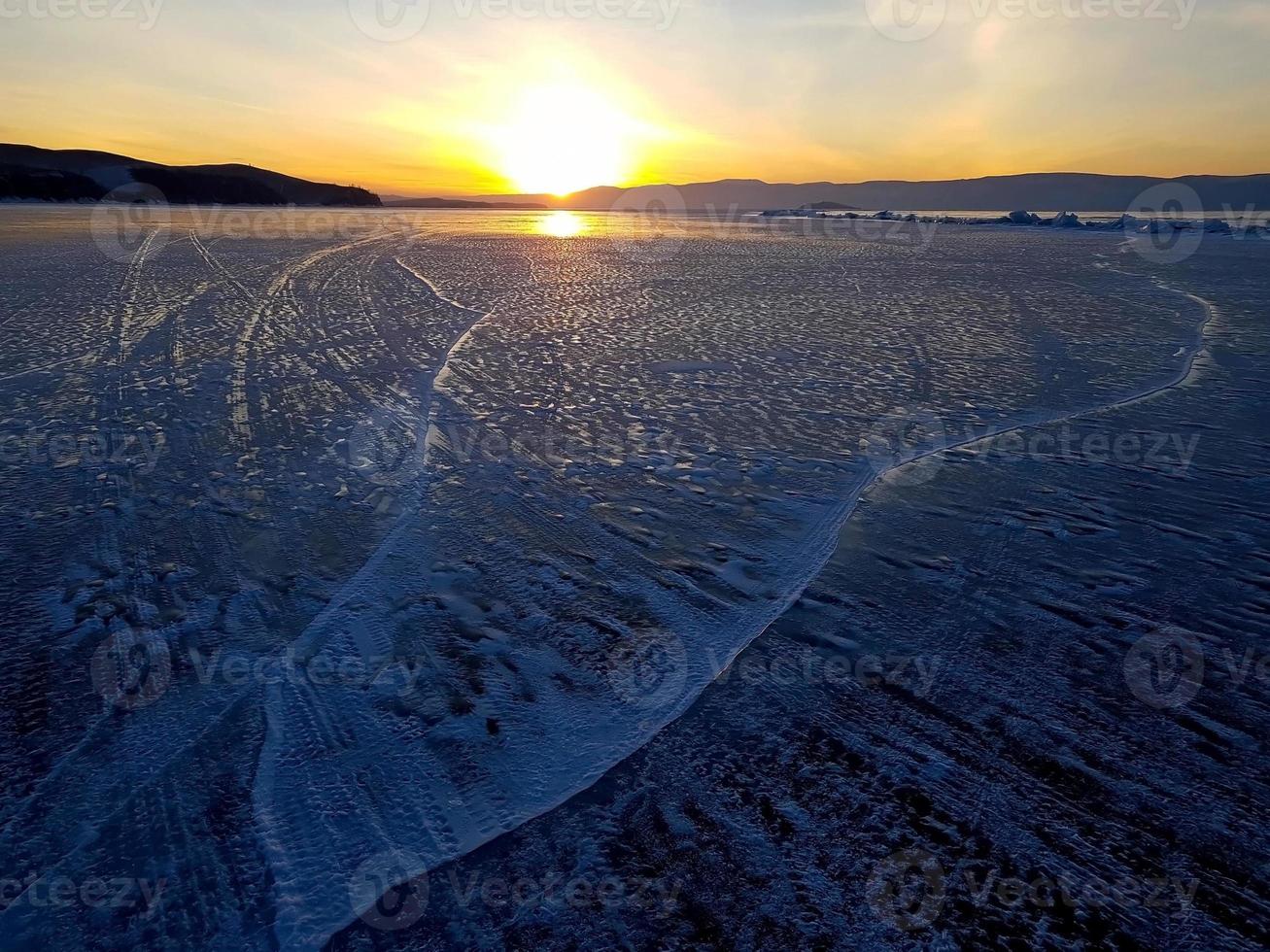 Beautiful sunset scene of Lake Baikal in winter, with texture and quaint pattern of tire tracks on ice surface. photo