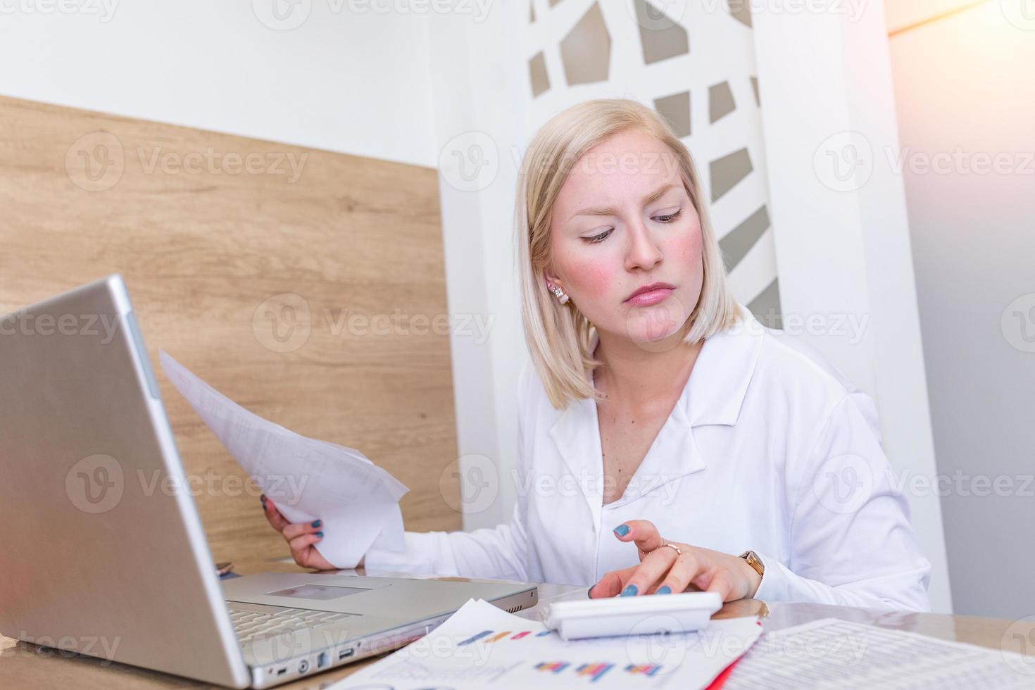 Serious focused businesswoman with laptop holding papers preparing report analyzing work results, female executive doing paperwork at workplace using computer online software for data analysis photo