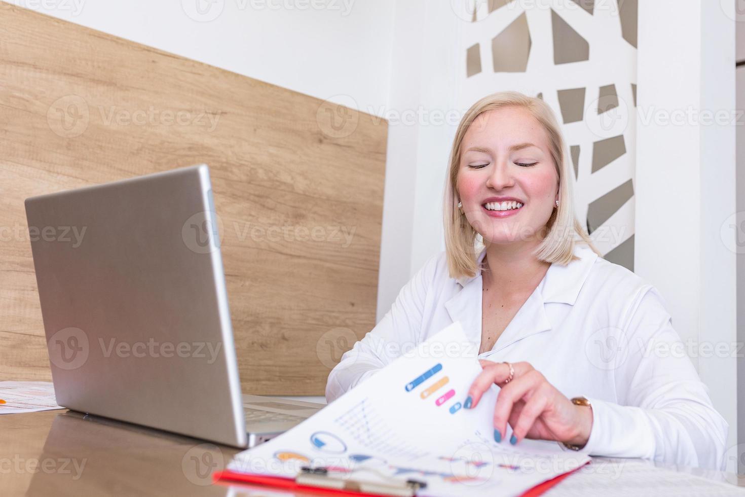 Portrait of smiling pretty young business woman sitting on workplace in office. Young albino woman working on her laptop in office photo