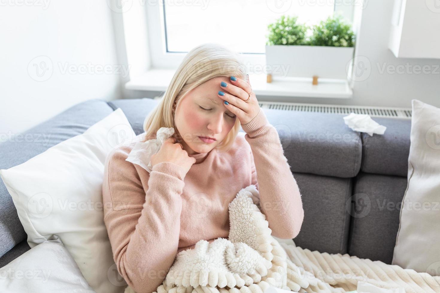 Sick woman with headache sitting under the blanket. Sick woman with seasonal infections, flu, allergy lying in bed. Sick woman covered with a blanket lying in bed with high fever and a flu, resting. photo