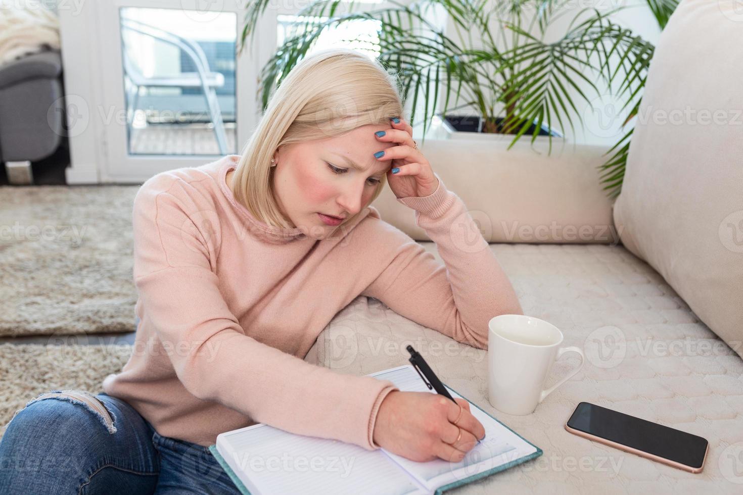 Girl studying the day before the exam, writing notes with a pencil. Pretty young girl doing her studies at home sitting on the floor in the living room with a book reading a binder of class notes photo