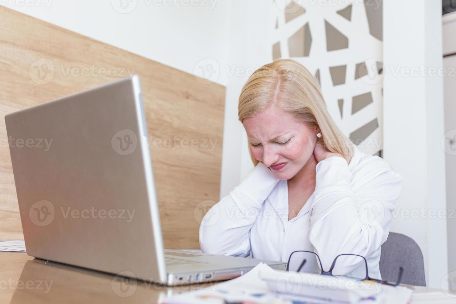 mujer de negocios siente dolor en el cuello después de sentarse en la mesa con una computadora portátil. mujer cansada que sufre del síndrome de la oficina debido a largas horas de trabajo en la computadora. linda chica masajeando sus tensos músculos del cuello foto