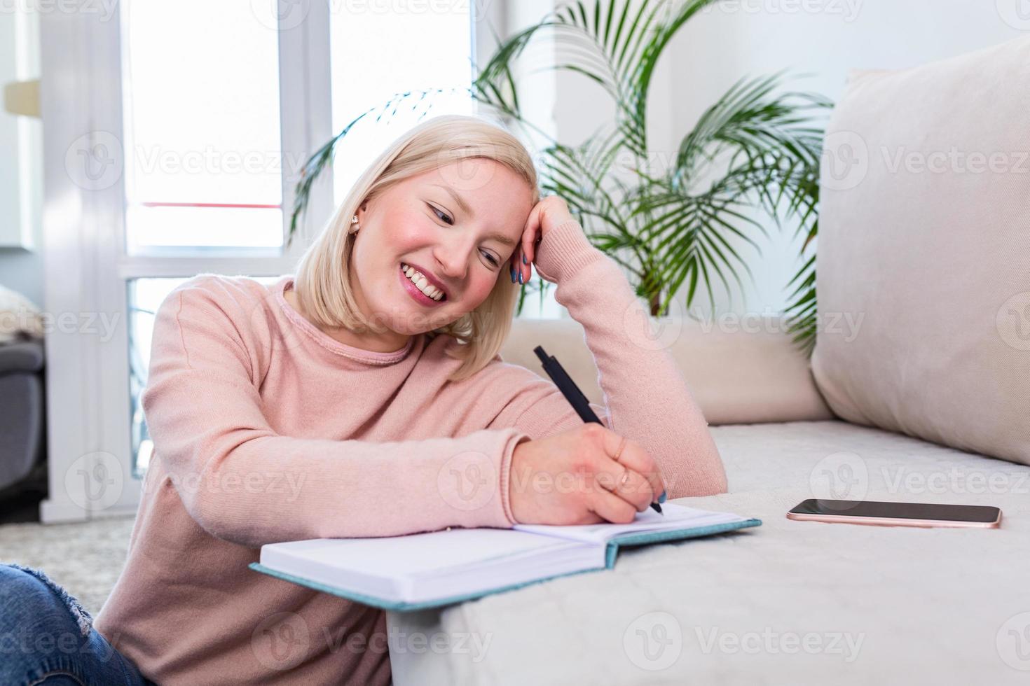 Girl studying the day before the exam, writing notes with a pencil. Pretty young girl doing her studies at home sitting on the floor in the living room with a book reading a binder of class notes photo