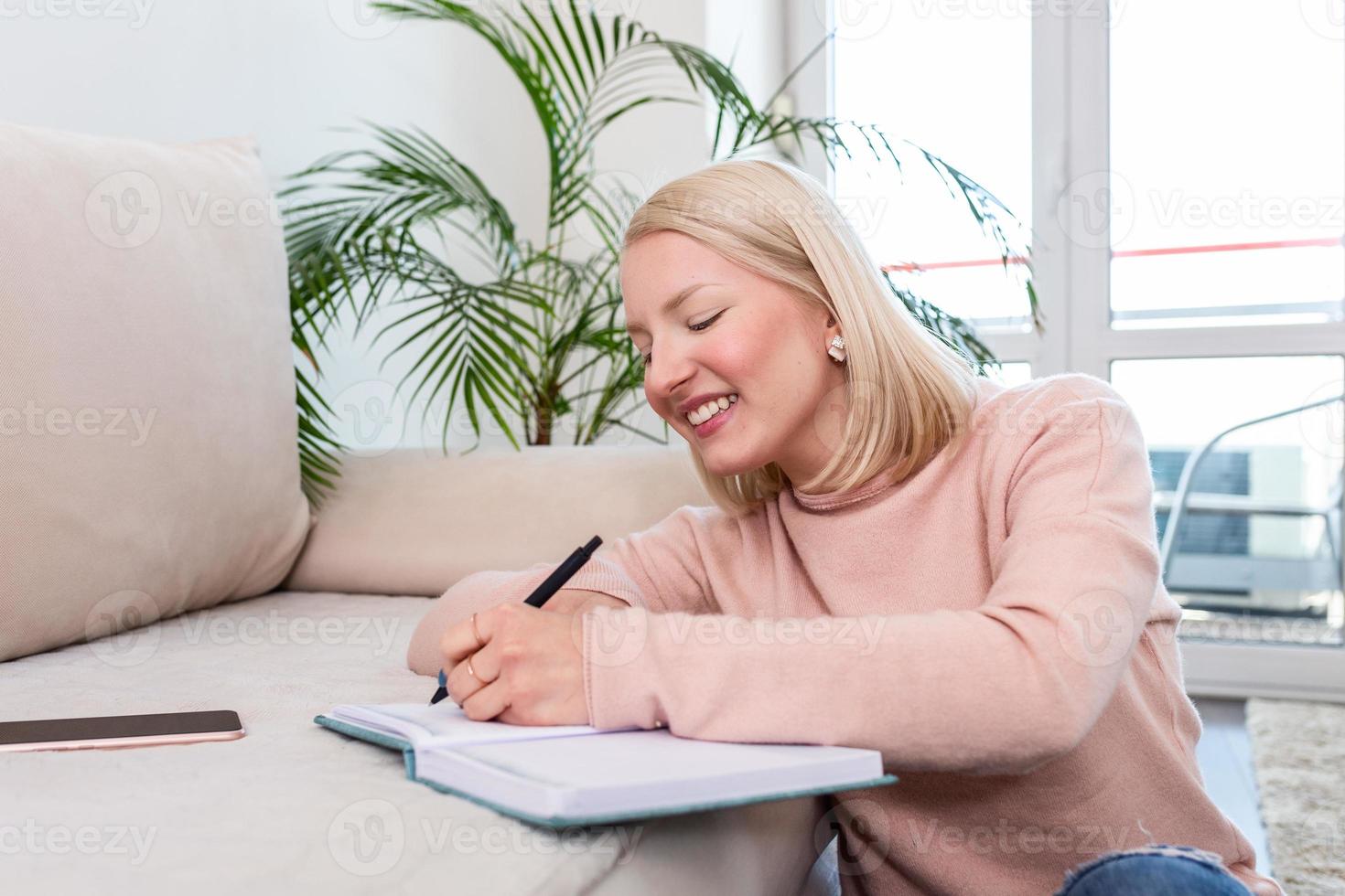 feliz mujer albina sentada en el suelo enmoquetado mientras estudiaba sus lecciones usando un libro con notas. empresario o estudiante trabajando o estudiando en casa y escribiendo notas sentadas en el suelo en casa foto