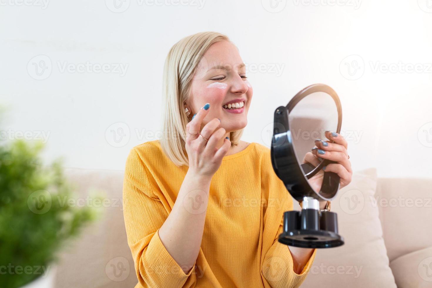 Young woman putting on moisturizer on her facial. Smiling young albino woman applying cream to face and looking to mirror. Cute woman putting anti-aging cream on her face photo