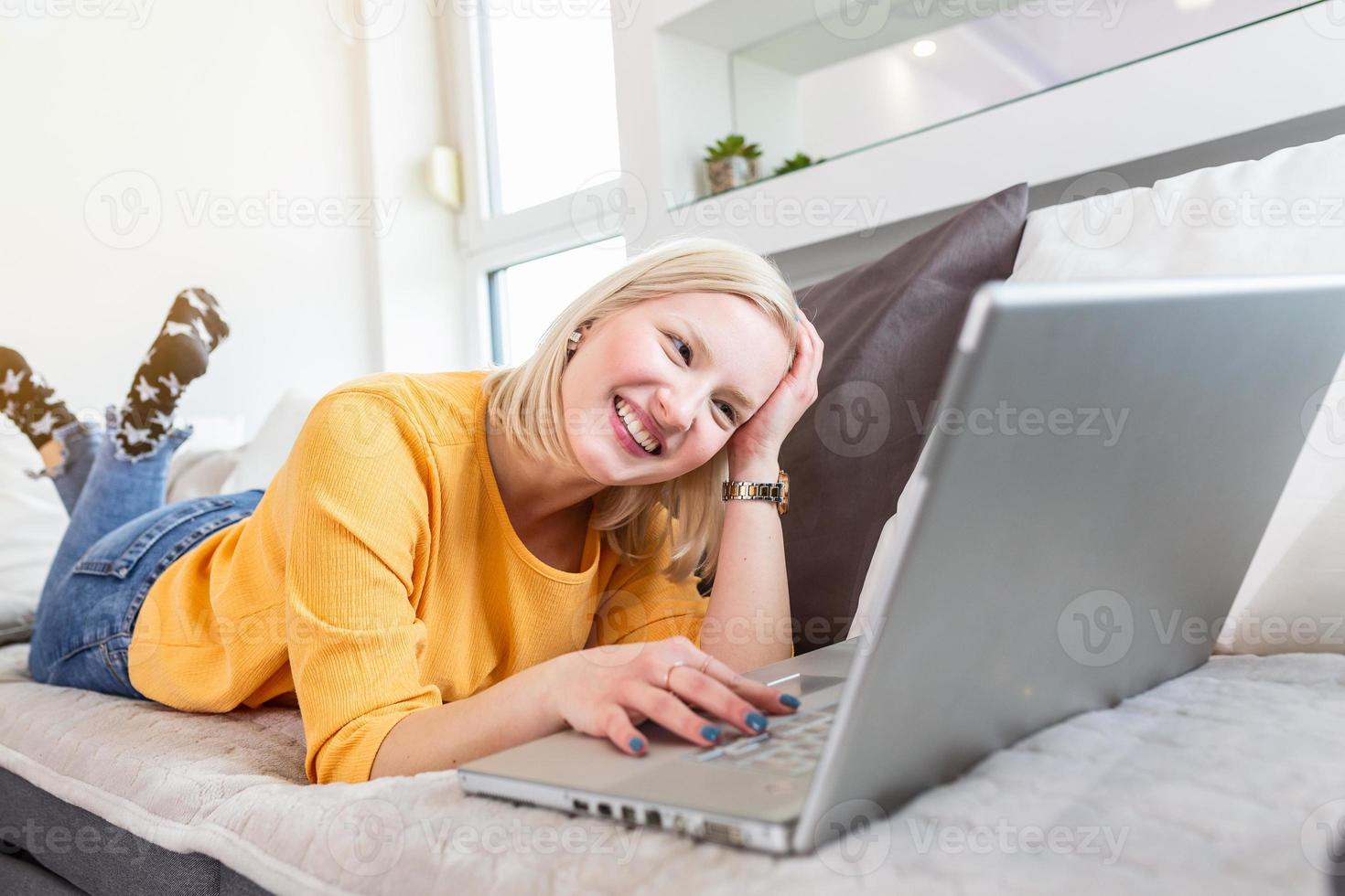 Smiling albino woman working from home, typing email on laptop, sitting on sofa. Surfing web at home. Side view of attractive young woman working on laptop and smiling while sitting on the couch photo