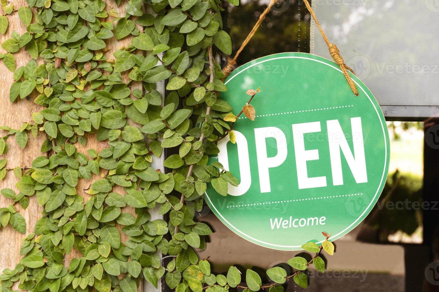 Hanging green sign with message OPEN on window with leaves ivy on wooden wall at coffee shop photo