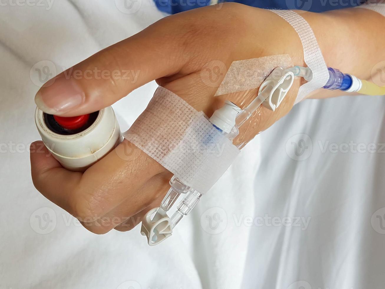 Macro image of patient hand with infusion needle and intra-veinous tube for intravenous infusion set on hand pushing emergency button at bed. photo