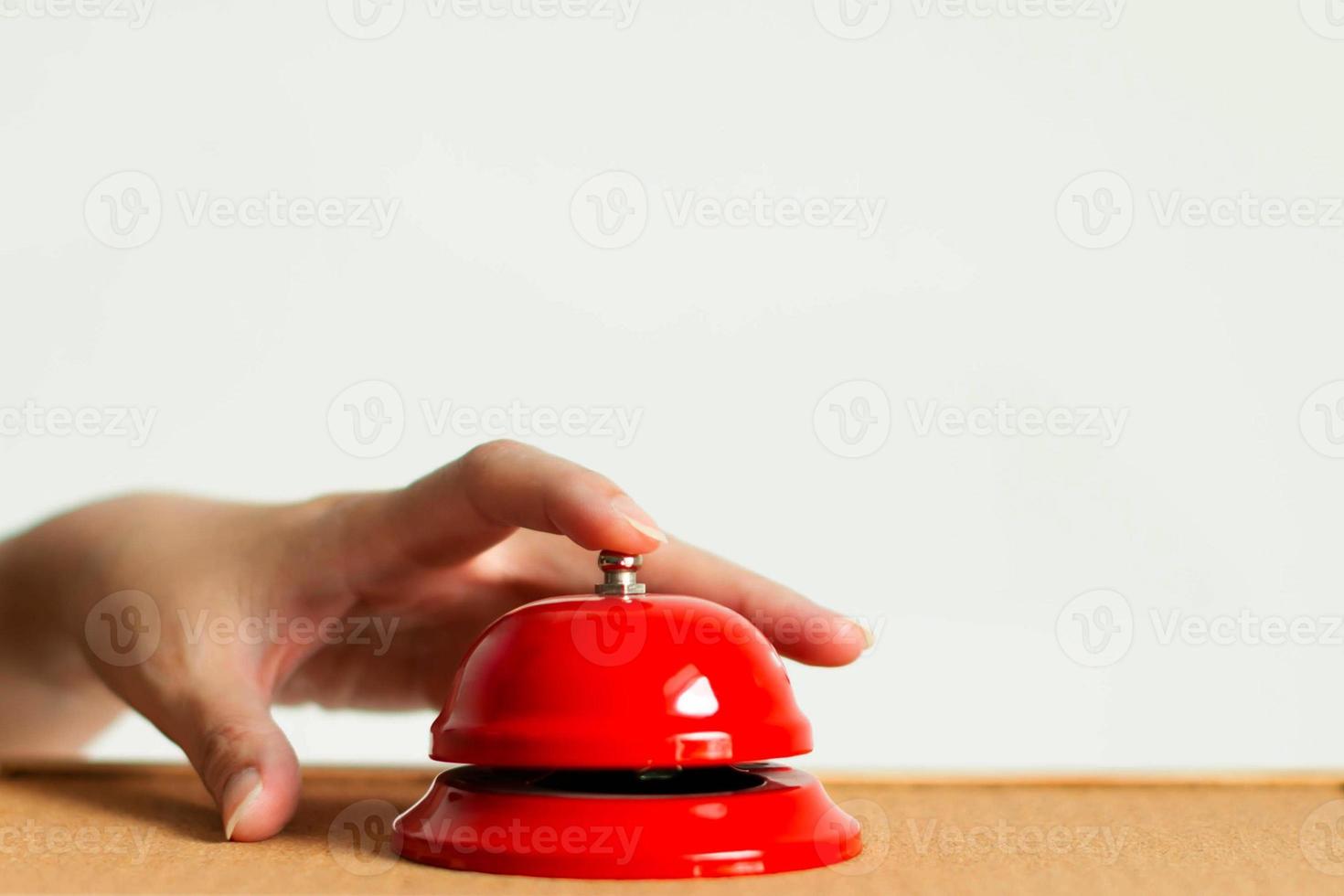 A hand using index finger pressing the bell button of red vintage style handbell on wooden surface in close-up. photo