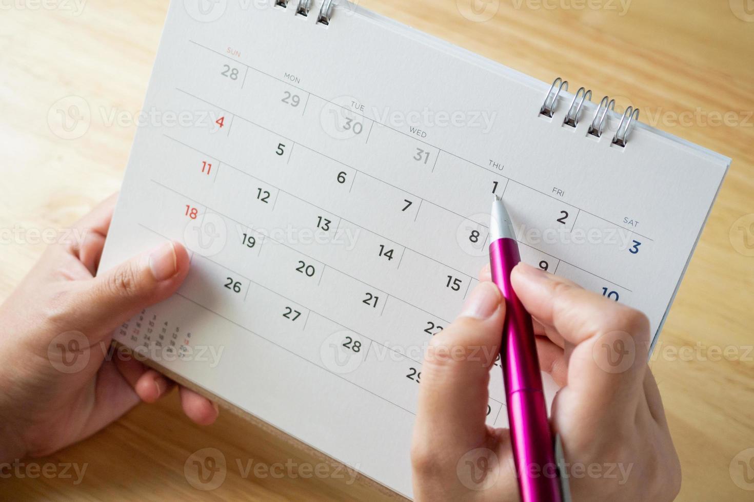 calendar page with female hand holding pen on desk table photo