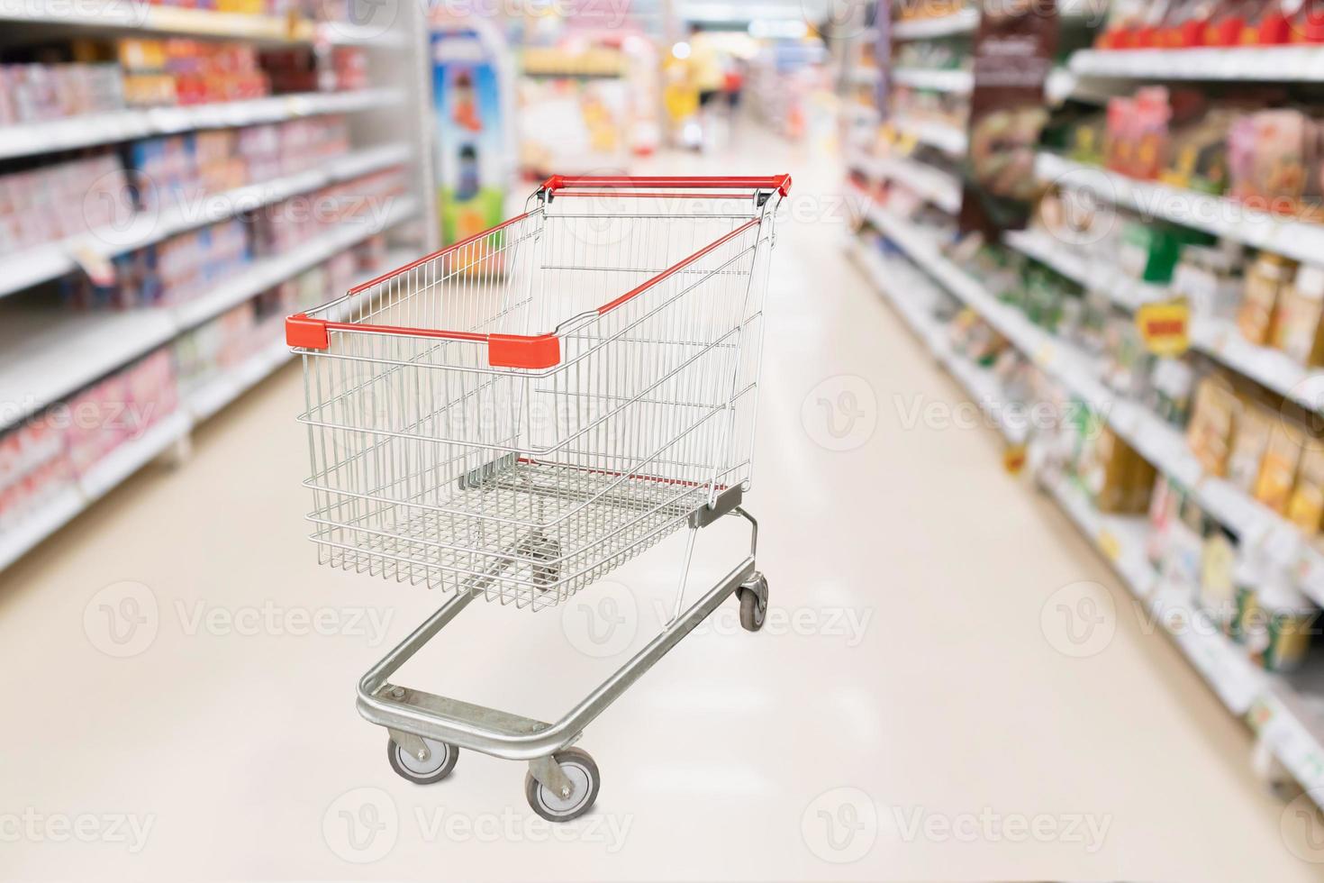 Supermarket aisle blurred background with empty red shopping cart photo