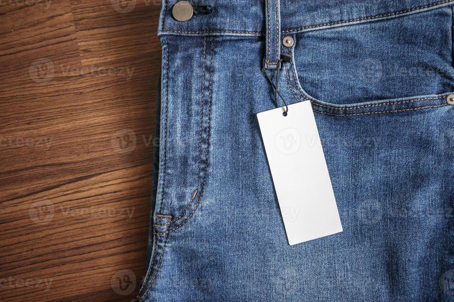 Blue jeans with blank white price label tag on wooden background photo