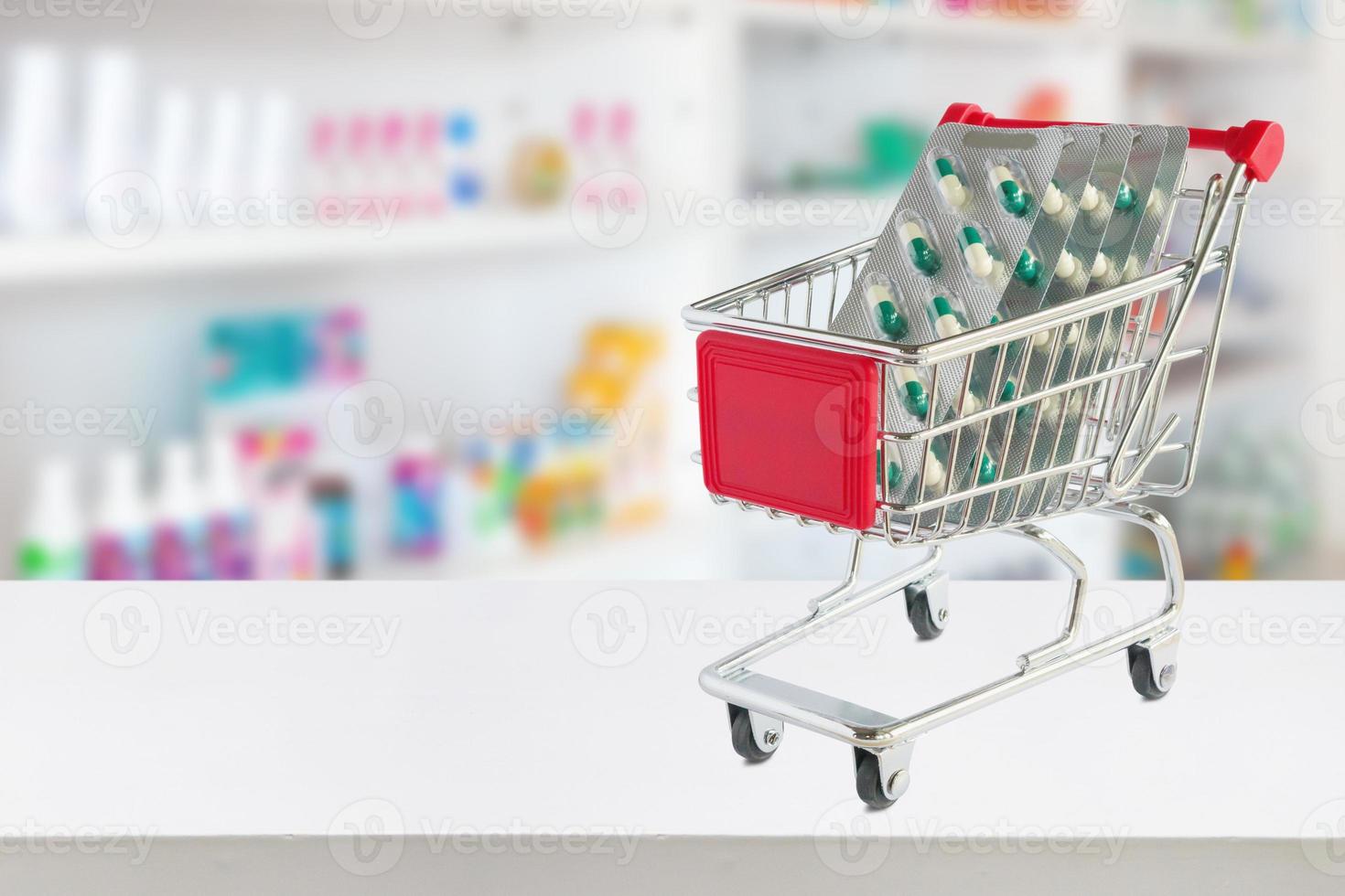 medicine pills capsule in shopping cart on pharmacy store counter with blur drugstore shelves defocused background photo