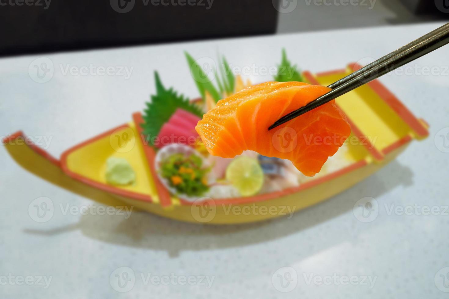 salmon in chopsticks with japanese sashimi set on boat plate photo