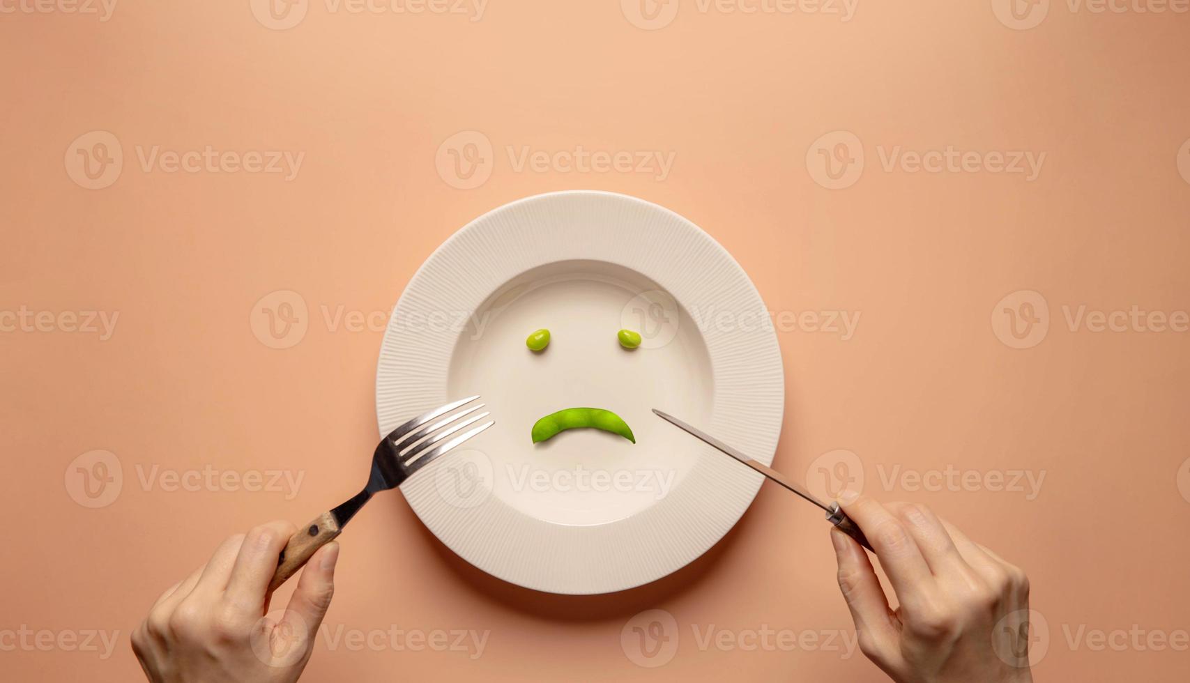 Diet and Health Care Concept. Try to Lose Weight. Young Woman Using Fork and Knife to Eating Green Soy Bean on Plate.  Unhappy Food. Top View photo
