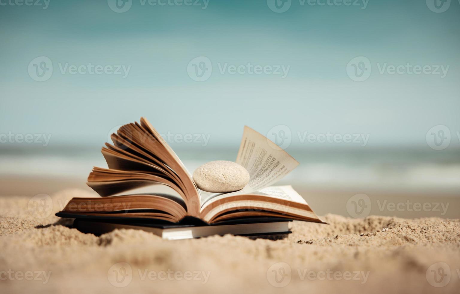 Reading Book Outdoor in Summer Concept. Opened Book on the Beach Sand in front of the Sea on Sunny Day. Lifestyle on Vacation photo