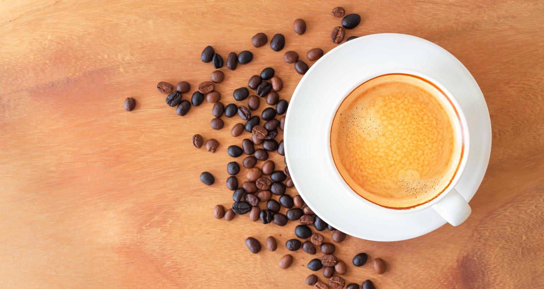 la vista superior de la taza de café tiene espuma dorada y granos de café mezclados o mezclados en el fondo de madera foto