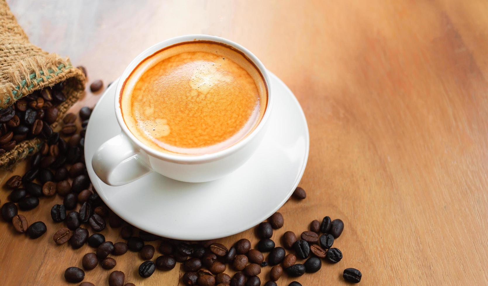 Top view of coffee cup has golden foam and mixed or blend coffee beans in a brown sack on wooden backgrou photo