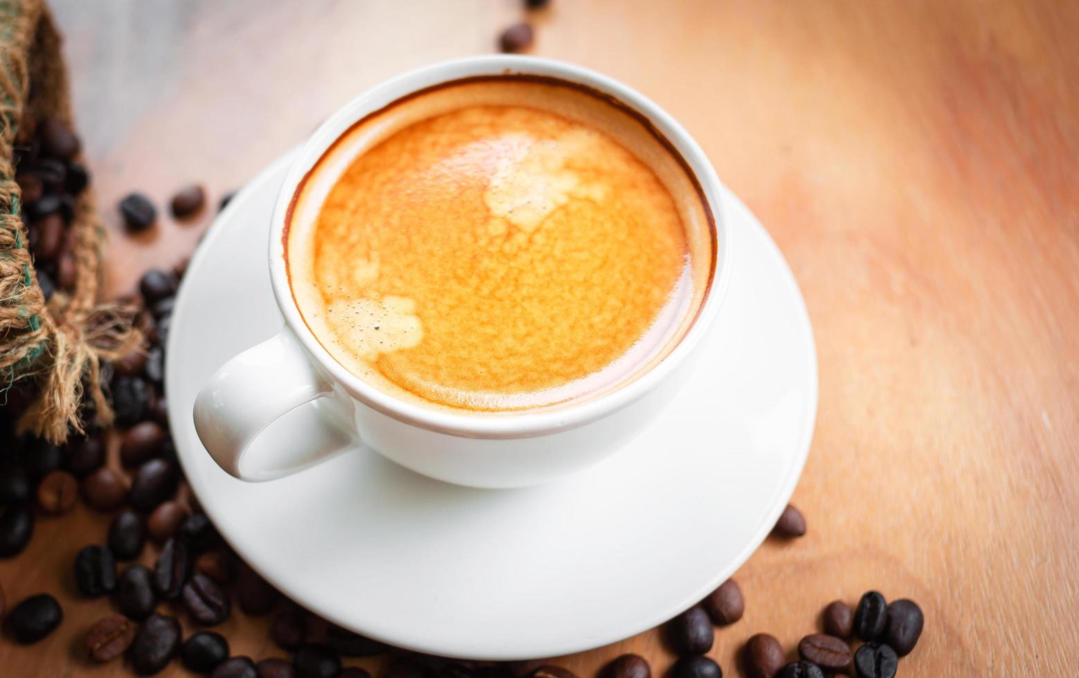 Close-up of a cup of latte with golden foam and mixed or blend coffee beans in a brown sack on an old wooden floor, top view. photo