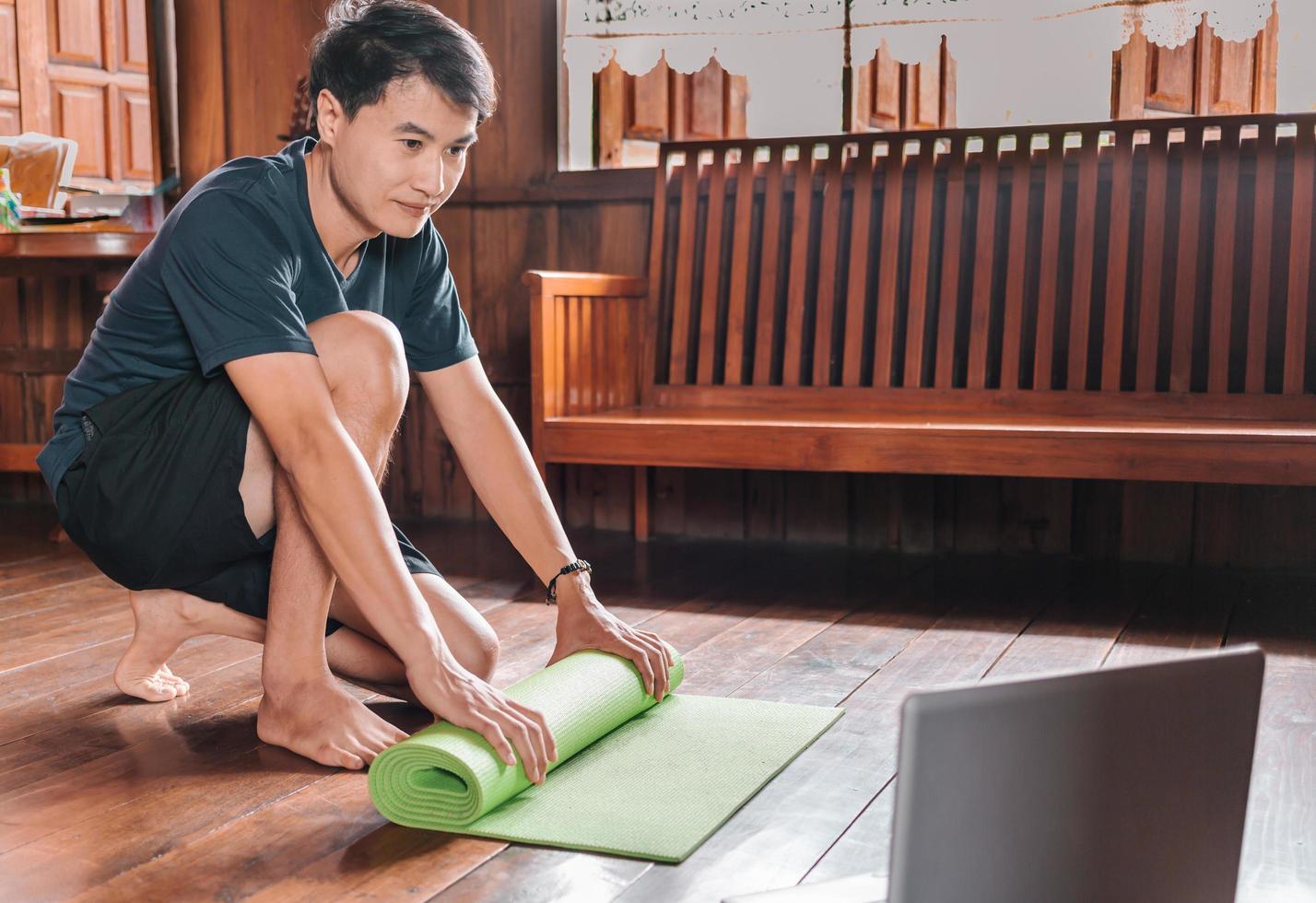 el primer plano de las manos de un hombre asiático está enrollando una colchoneta de ejercicios y preparándose para hacer yoga. él está haciendo ejercicio en un piso o alfombra bajo el sol de la mañana en casa. concepto de estilo de vida saludable. foto