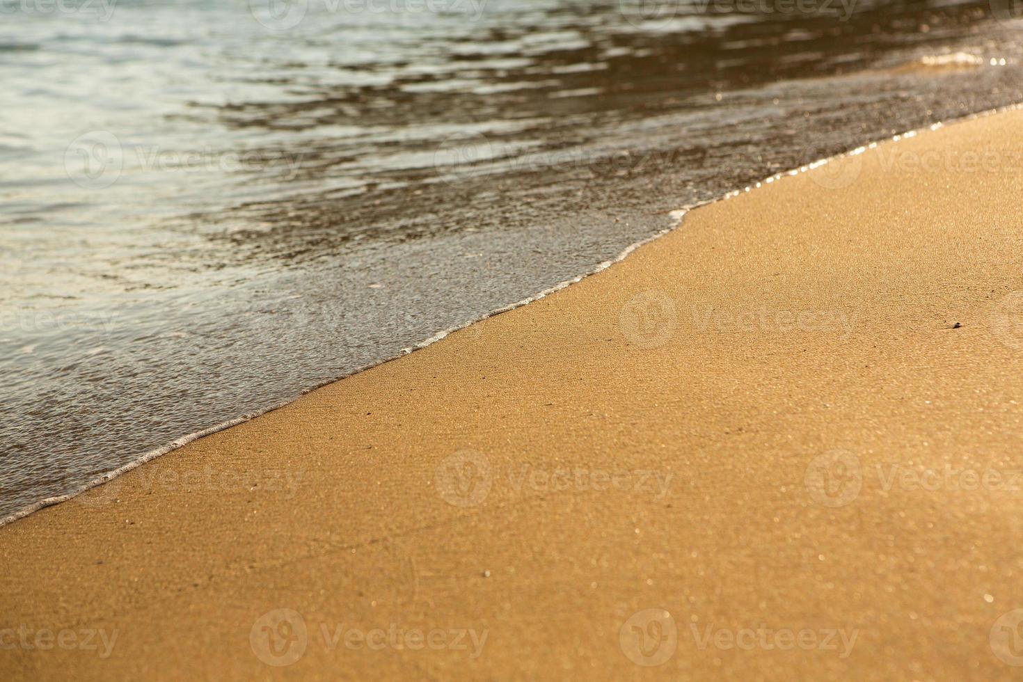 Background with golden sand on the coast of the island of Crete. Abstract surface with sand and clear sea water for text. photo