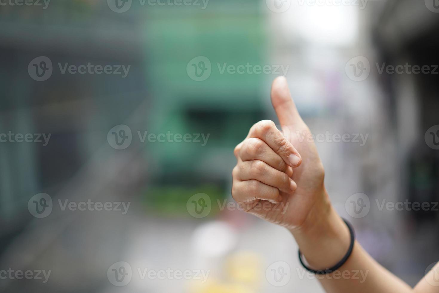 Women raise up the thumb with blur green background near sky train, Bangkok, Thailand. photo