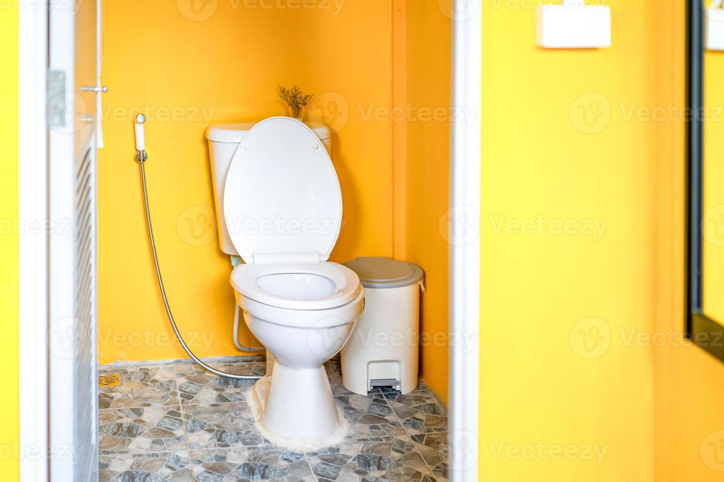 Yellow Toilet room with flush toilet, tash and toilet paper inside it. This is located in the garden. photo