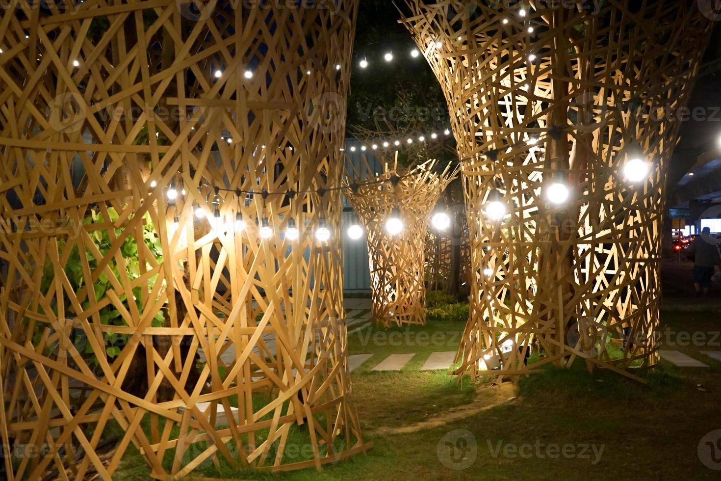 el arte decorado con grandes palos de madera se pega alrededor del árbol en la noche con luz de tungsteno colgando alrededor. foto