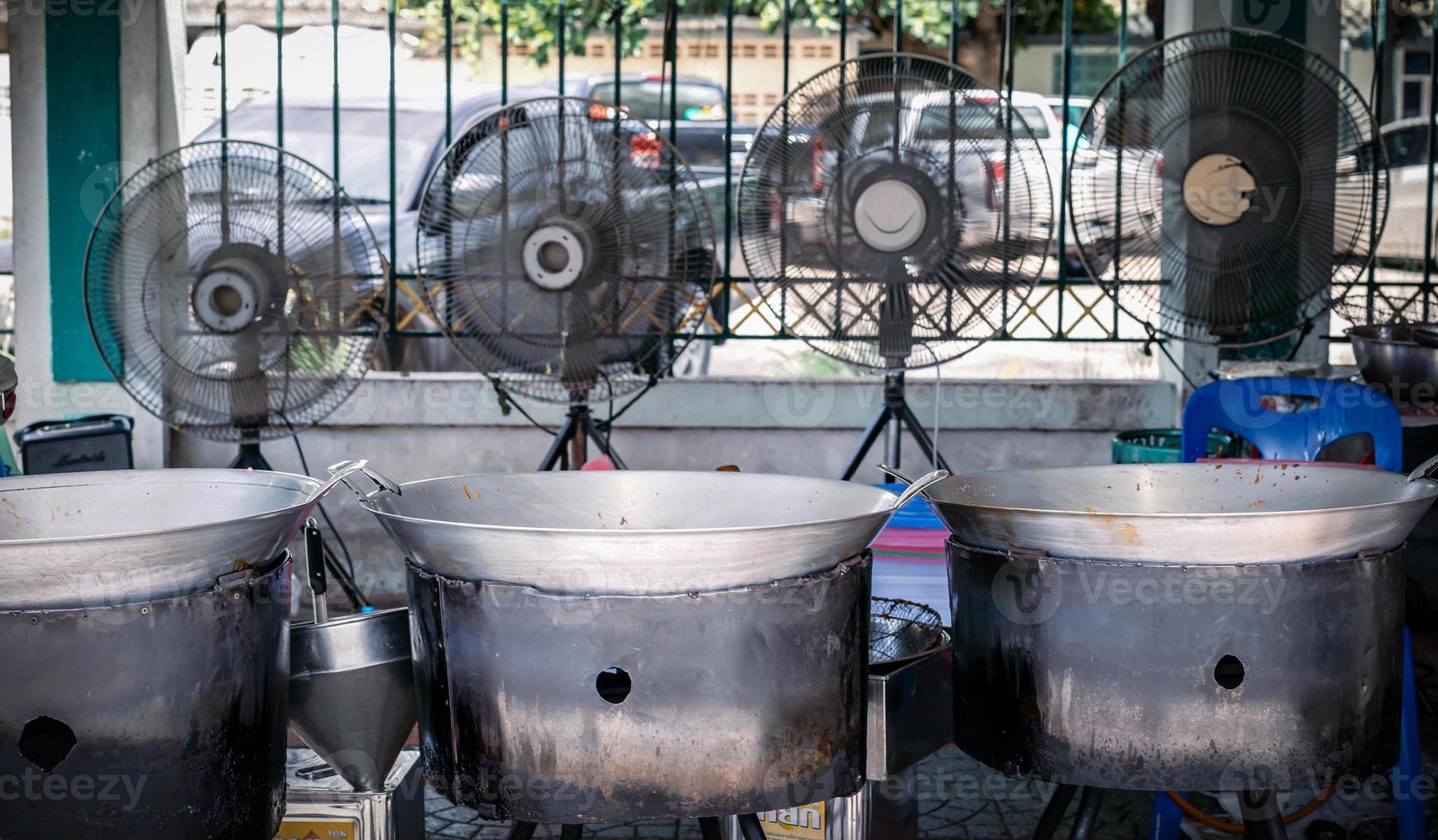 Three large Pans are fried the fried chicken with large three fan behind them. This is the street food Fried chicken booth at the footpath next to the road. photo