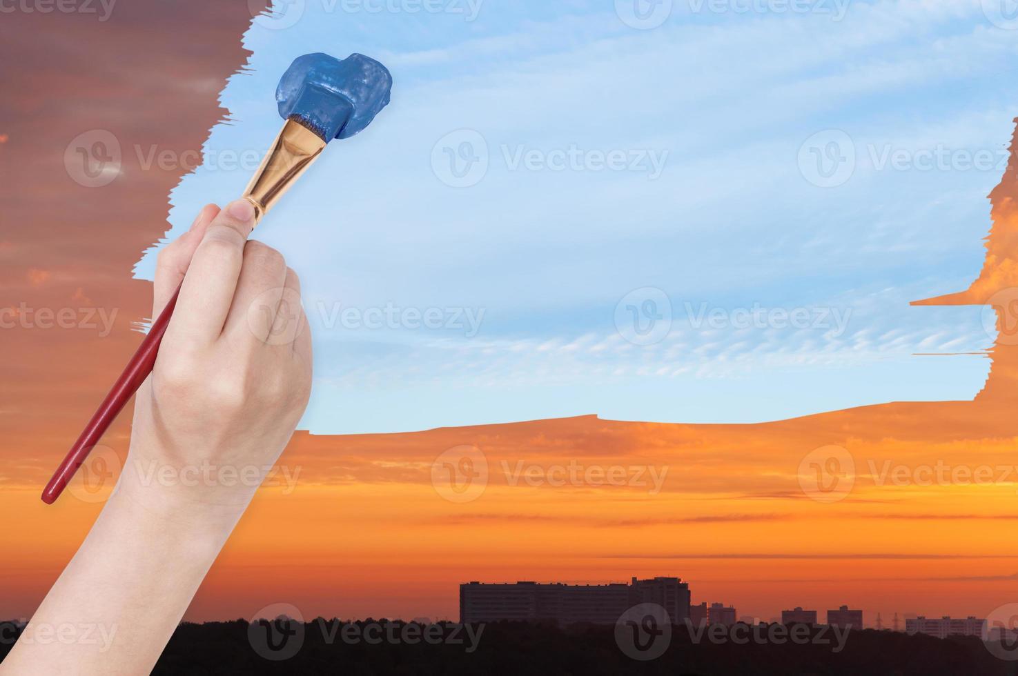 paintbrush paints blue day sky on orange sunset photo