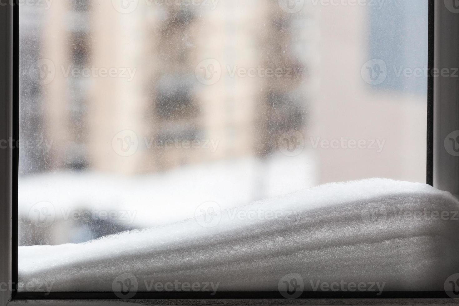 snow on window pane and houses on background photo