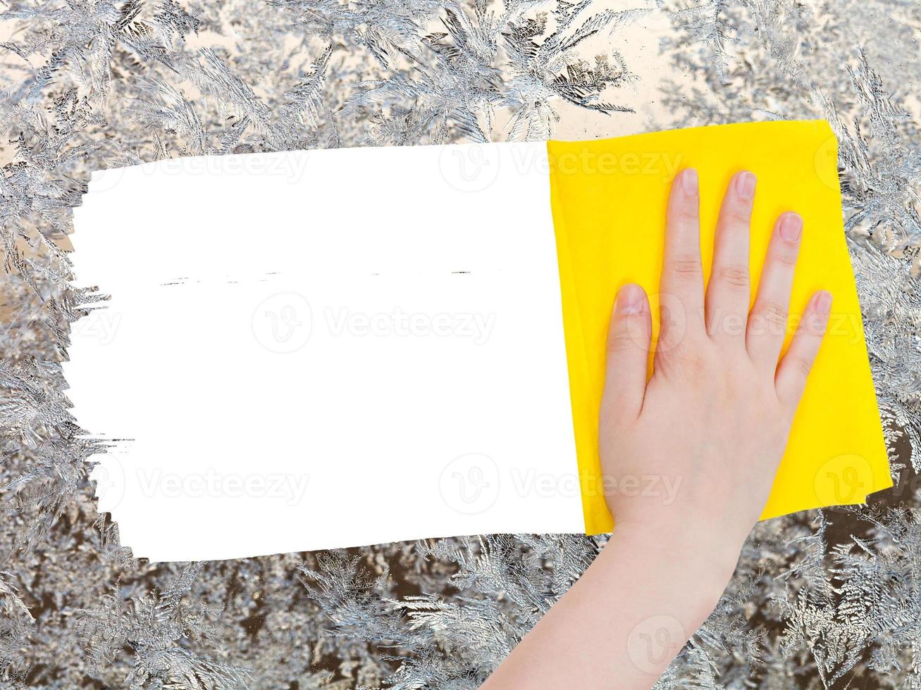 hand deletes frozen pattern on glass by yellow rag photo