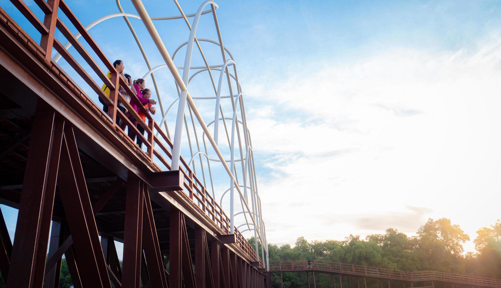 Group of Asian women in workout clothes Standing on a wooden bridge in the park in the morning when the sun rises. Wooden bridge at Chedi Klang Nam, Rayong Province, Thailand photo