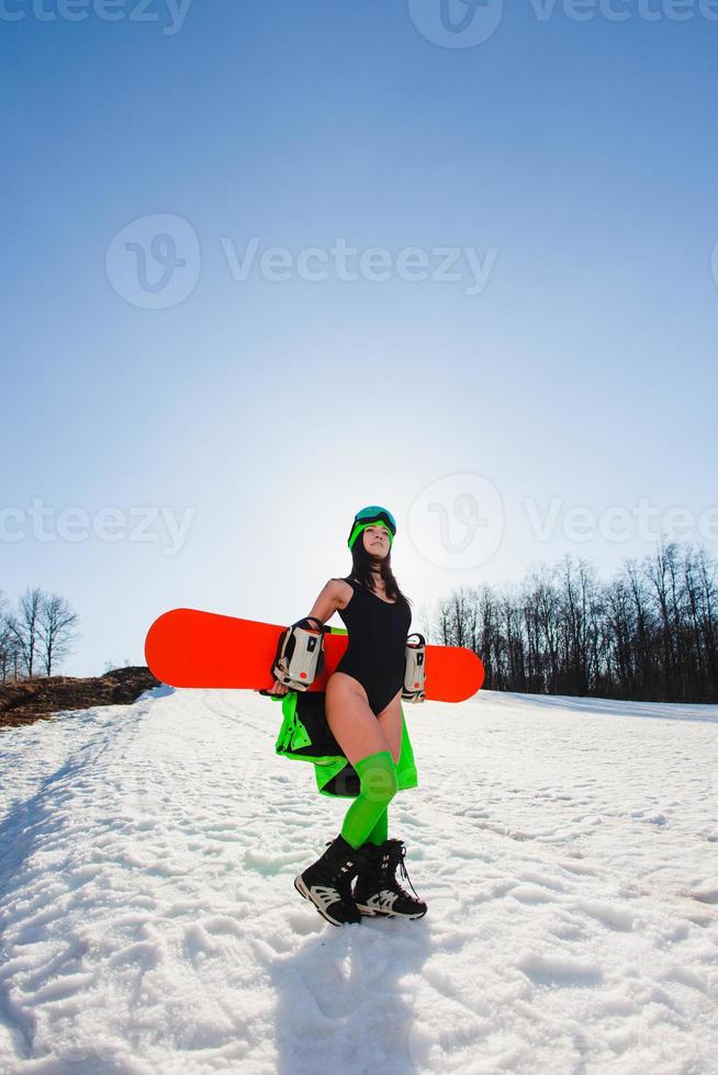 mujer hermosa joven posando con una tabla de snowboard en una pista de esquí foto