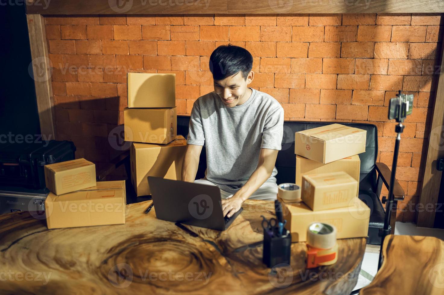 An Asian man uses a mobile phone to take orders and display items in a box that records live streaming video online at the store. small business owner Asian online market delivery concept photo