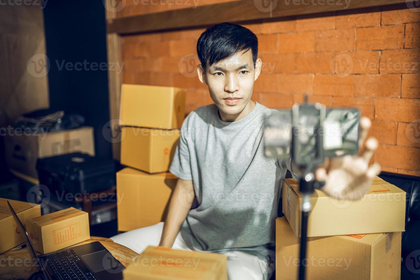 An Asian man uses a mobile phone to take orders and display items in a box that records live streaming video online at the store. small business owner Asian online market delivery concept photo