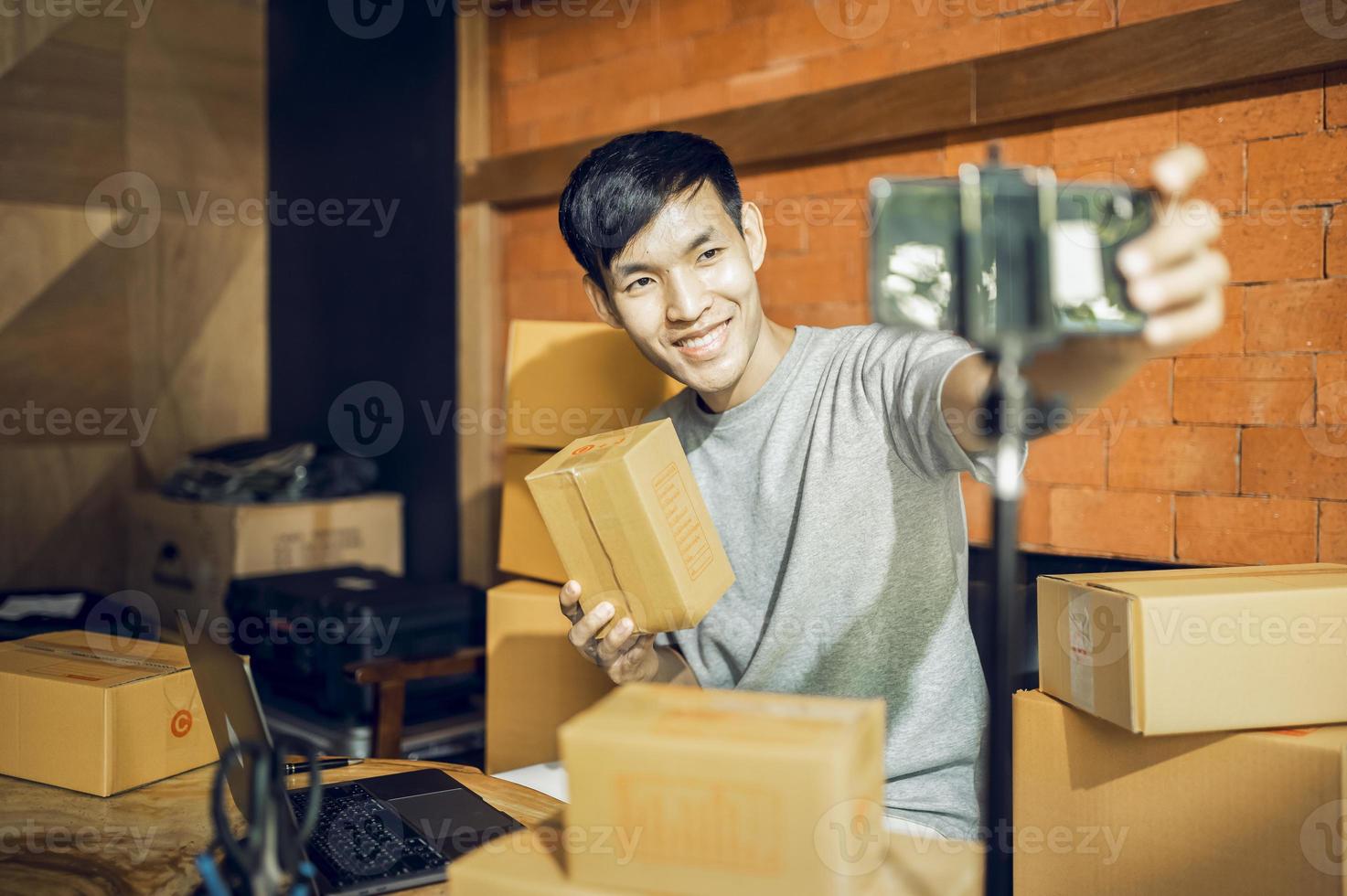 An Asian man uses a mobile phone to take orders and display items in a box that records live streaming video online at the store. small business owner Asian online market delivery concept photo