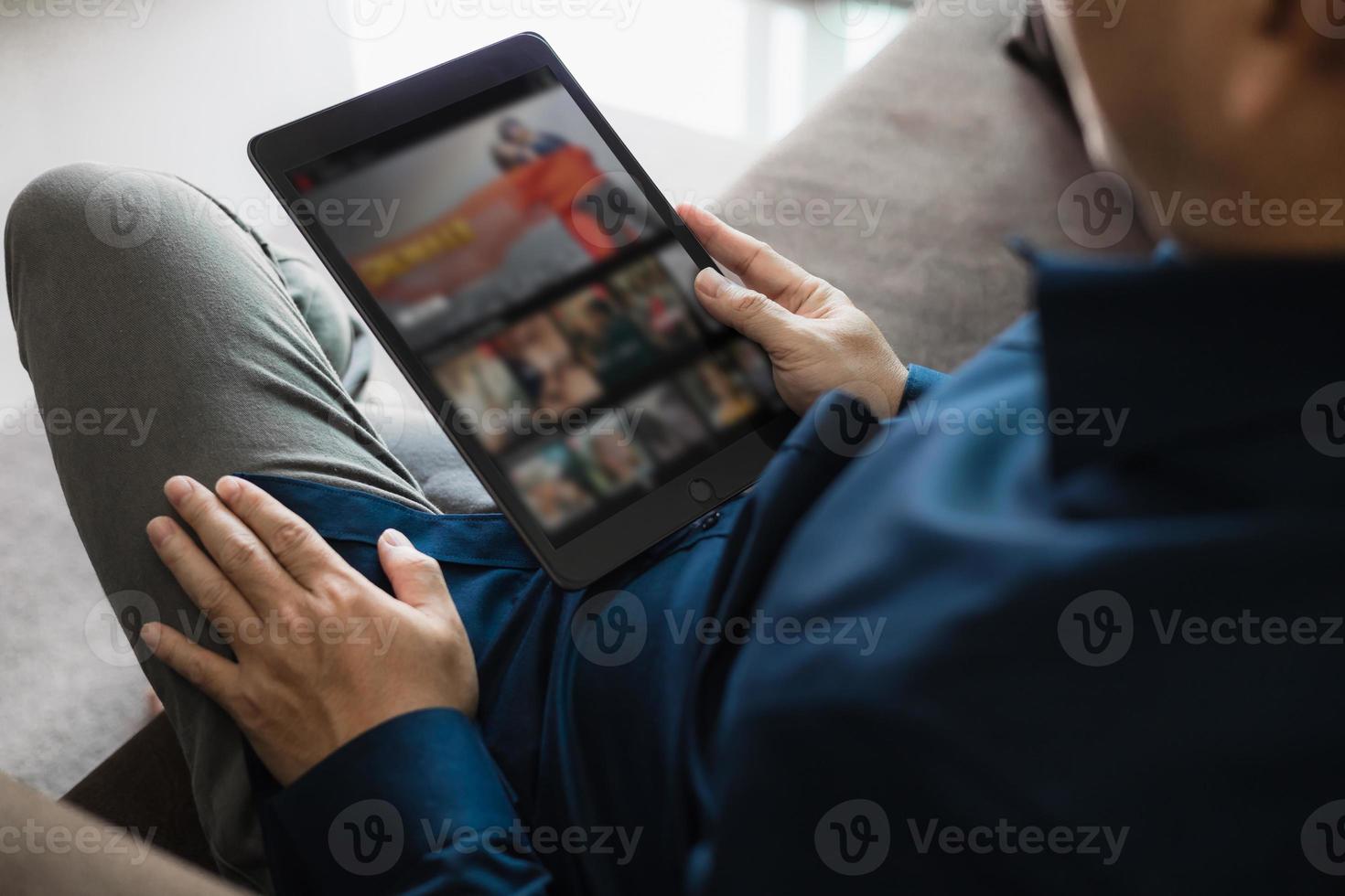 Dressed man watching video on tablet sitting on sofa in house photo