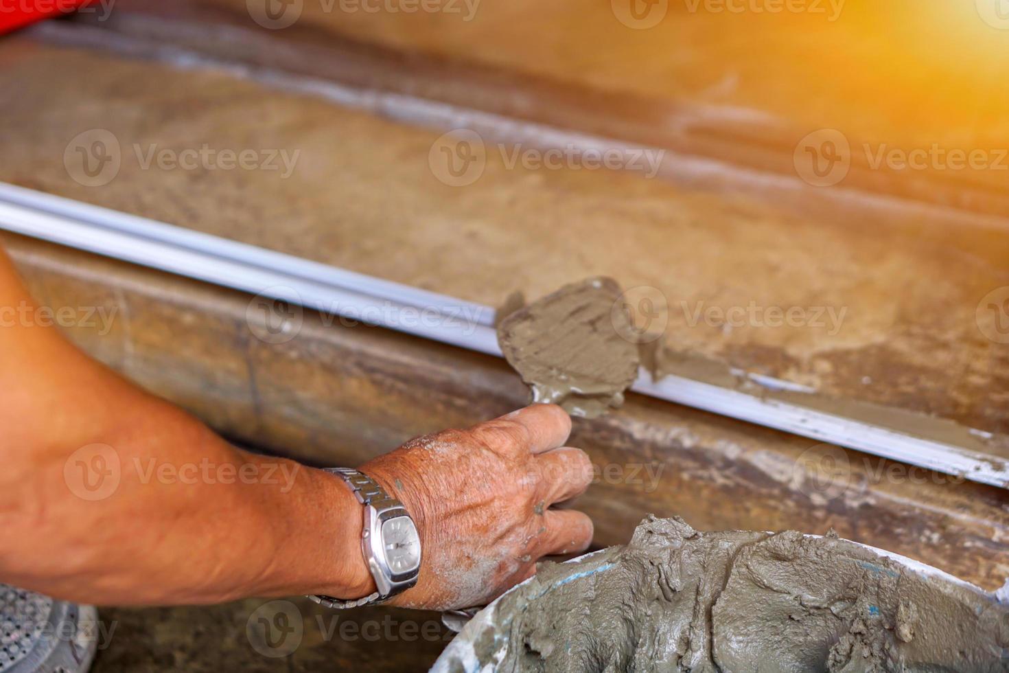 Closeup hands of laborer holding wood trowel working at construction site with sun flare background. photo