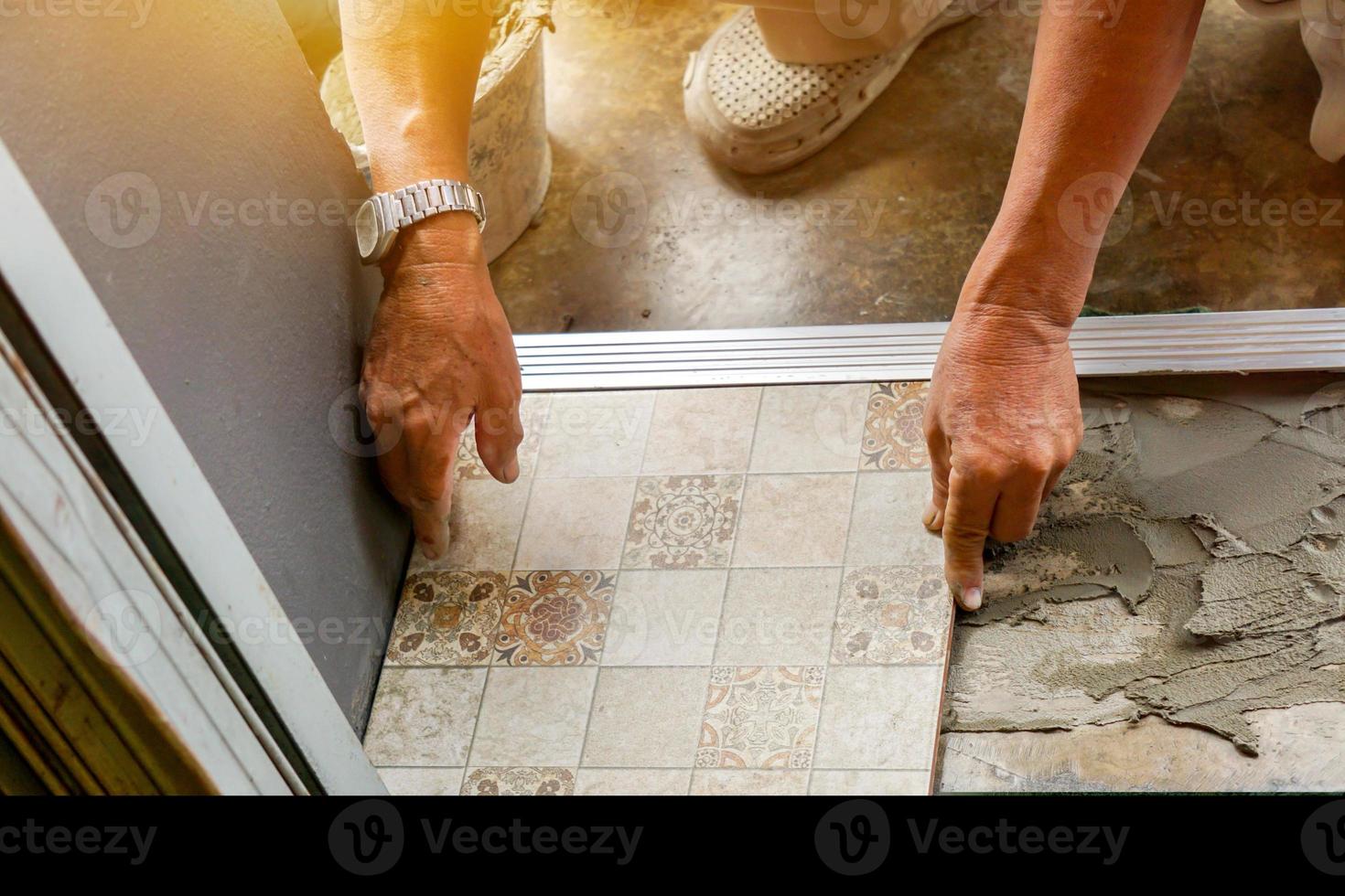 Closeup hands of laborer working install  tiled floor at construction site with sun flare background. photo